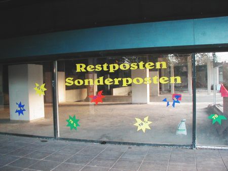 Entkerntes Geschäft, mit aufgeklebtem Werbetext im Fenster: Restposten, Sonderposten