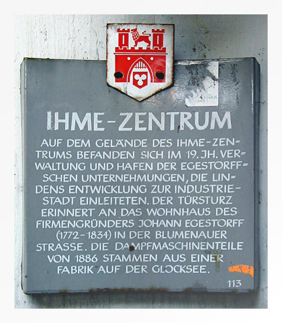 Schild, das im Ihmezentrum hing, bevor es von Carlyle zum Lindenpark umgebaut wurde, aber so, dass nur eine Ruine zurückblieb -- Ihme-Zentrum -- Auf dem Gelände des Ihme-Zentrums befanden sich im 19. Jh. Verwaltung und Hafen der Egestorffschen Unternehmungen, die Lindens Entwicklung zur Industriestadt einleiteten. Der Türsturz erinnert an das Wohnhaus des Firmengründers Johann Egestorff (1772-1834) in der Blumenauer Straße. Die Dampfmaschinenteile von 1886 stammen aus einer Fabrik auf der Glocksee